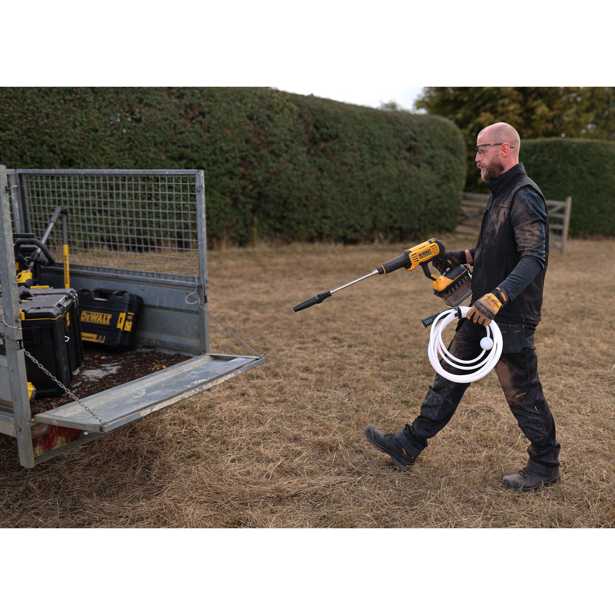 Man walking towards an open trailer holding the DEWALT 54V XR FLEXVOLT Power Cleaner with hose